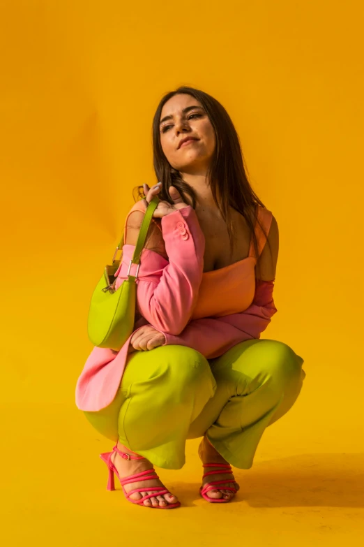 a woman sitting on the ground, wearing a pink and green outfit and holding a purse