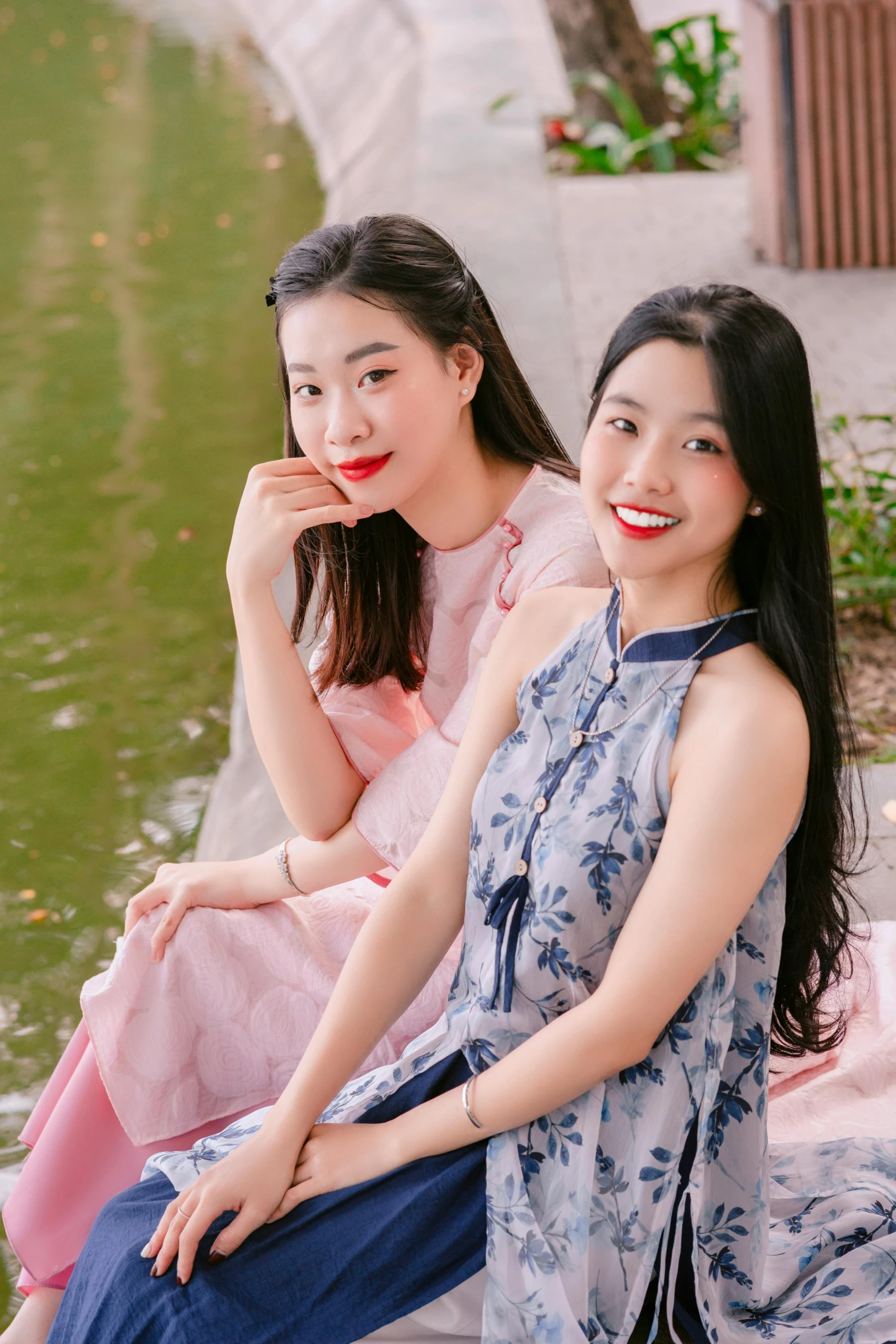 two women sitting on a concrete wall near water