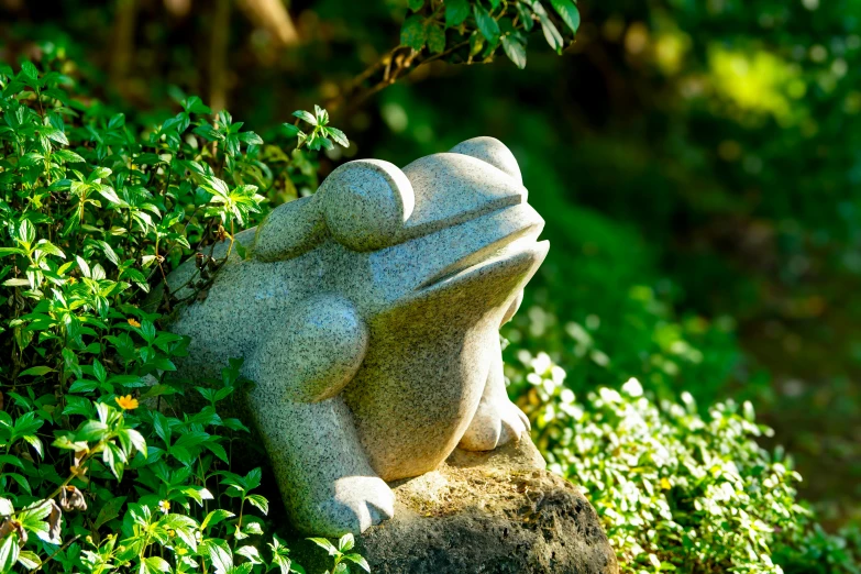 a frog sculpture in some bushes on a sunny day