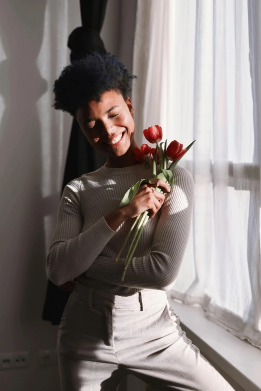 a woman is smiling holding some red flowers