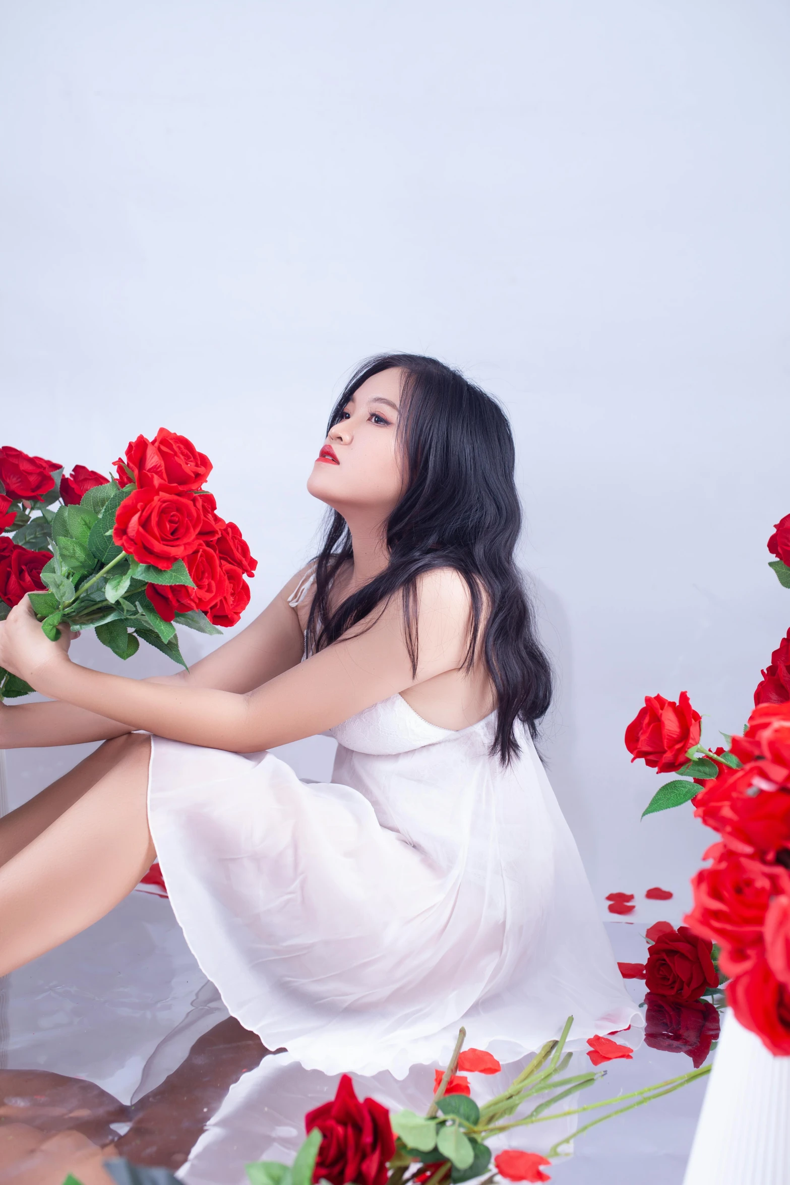 a young woman holding some red roses by her foot