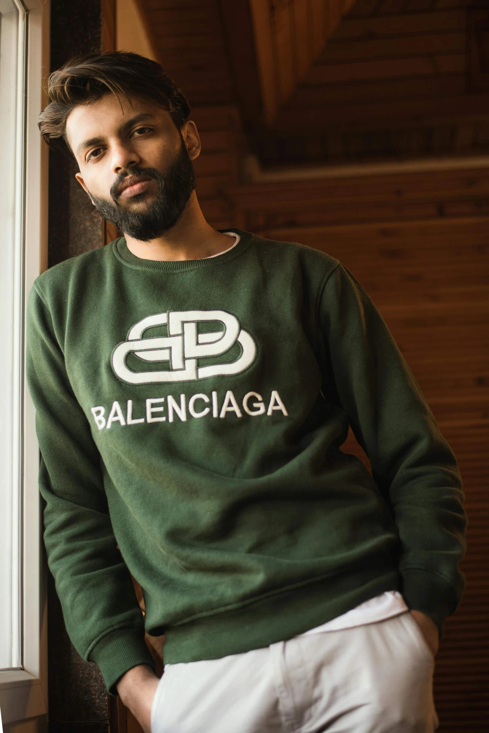 man in a green sweater stands near the window of a house