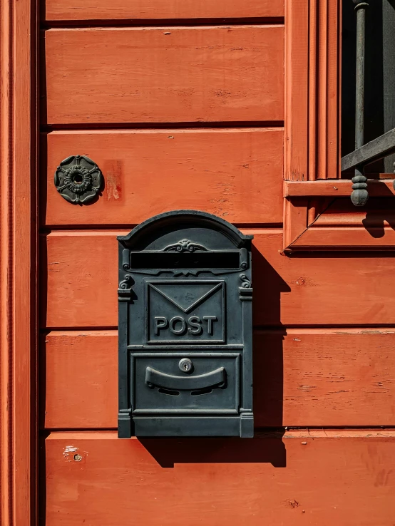 a black mailbox hanging on a red wooden wall