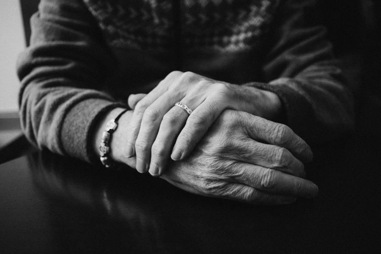 an old man holding his hands together at a table