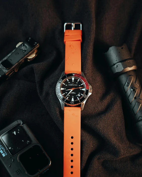 a orange watch with a silver case sitting next to two batteries