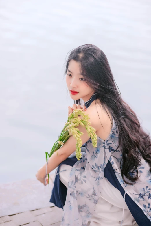 a beautiful young woman holding leaves by a body of water