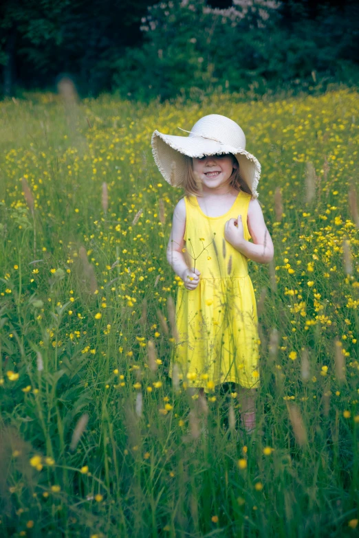 a little girl standing in a flower field wearing a hat