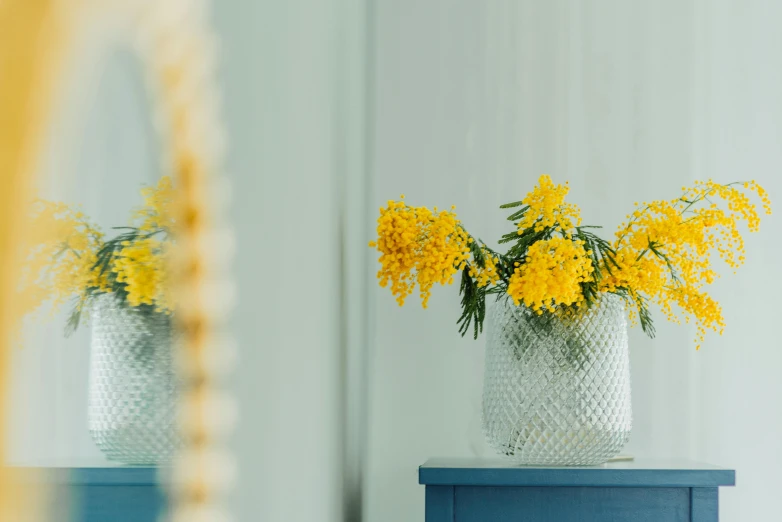 a mirror sitting next to a blue side table and two yellow flowers