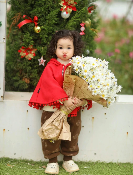 a little girl holding a bouquet of flowers standing on grass