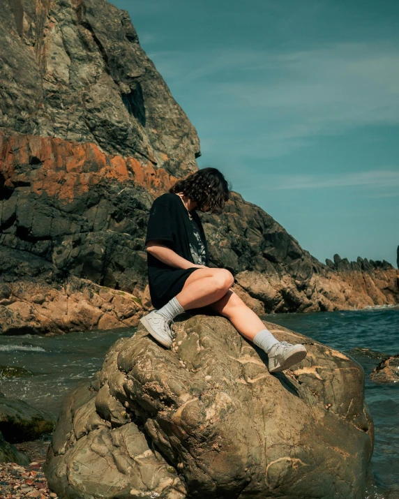 a woman sitting on top of a rock near a body of water