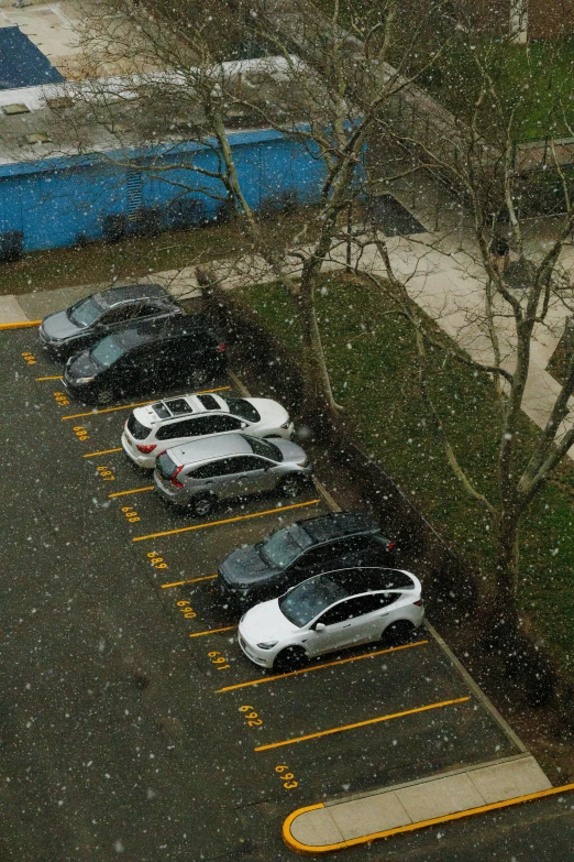 several parked cars sit in the snow in a parking lot