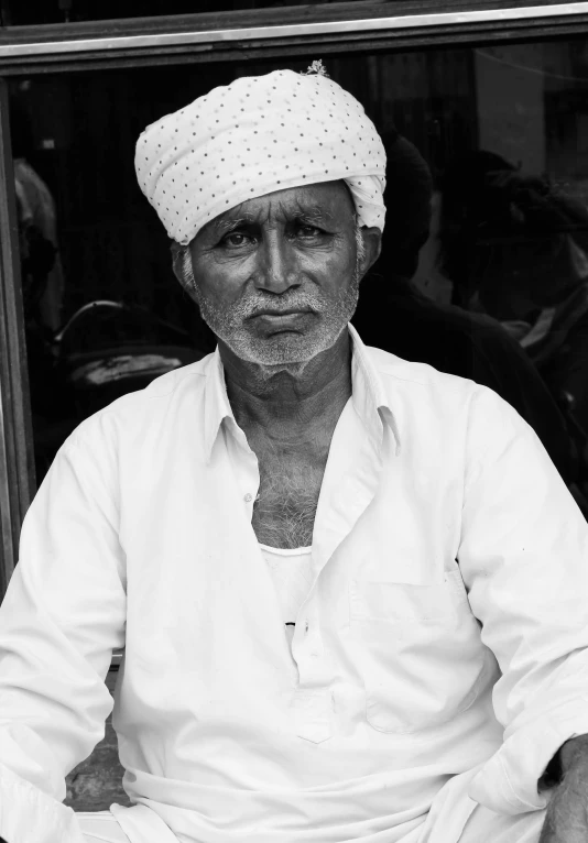 an old man with a turban is seated outside