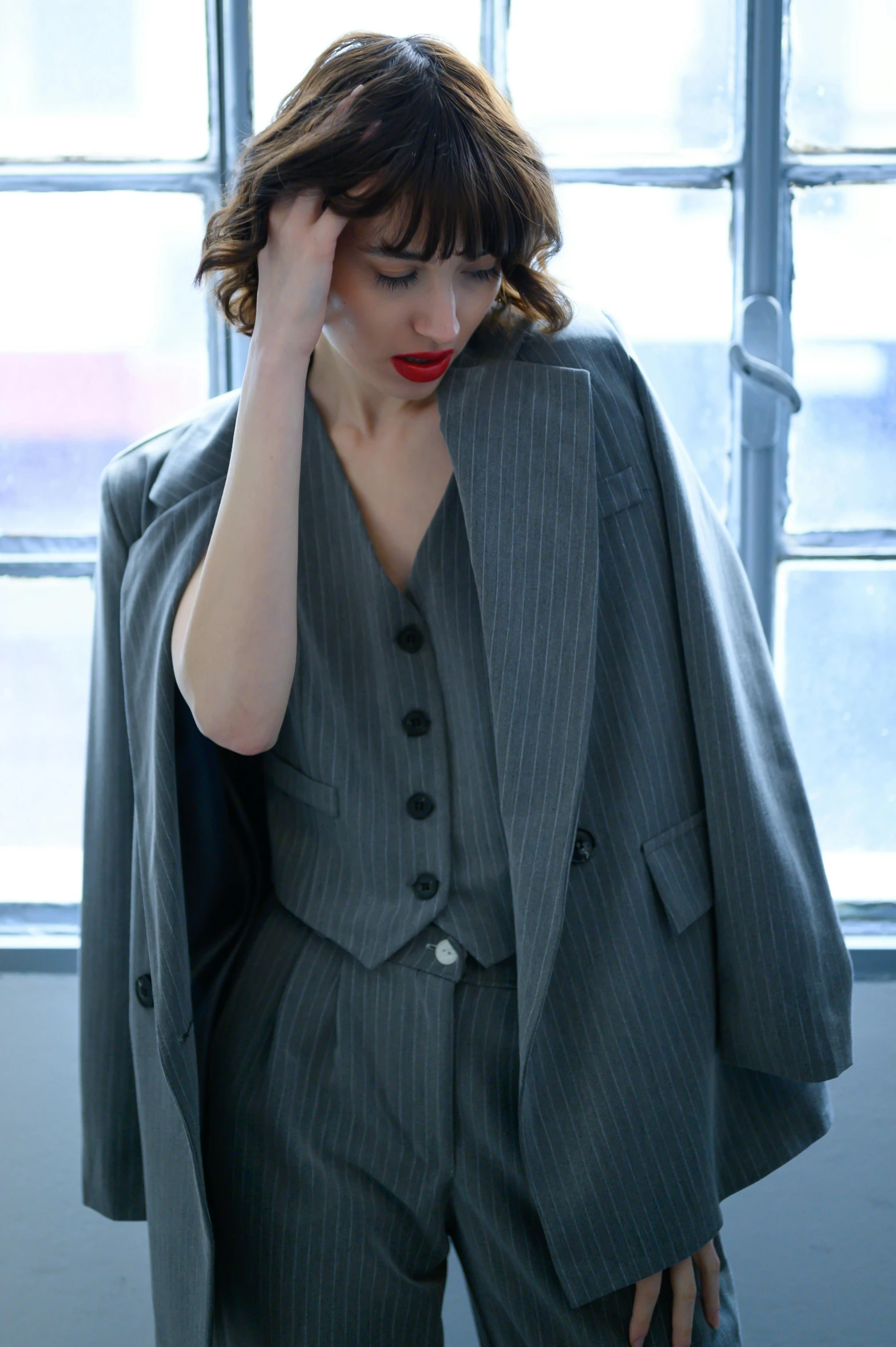 a woman wearing a suit and red lips standing next to some windows