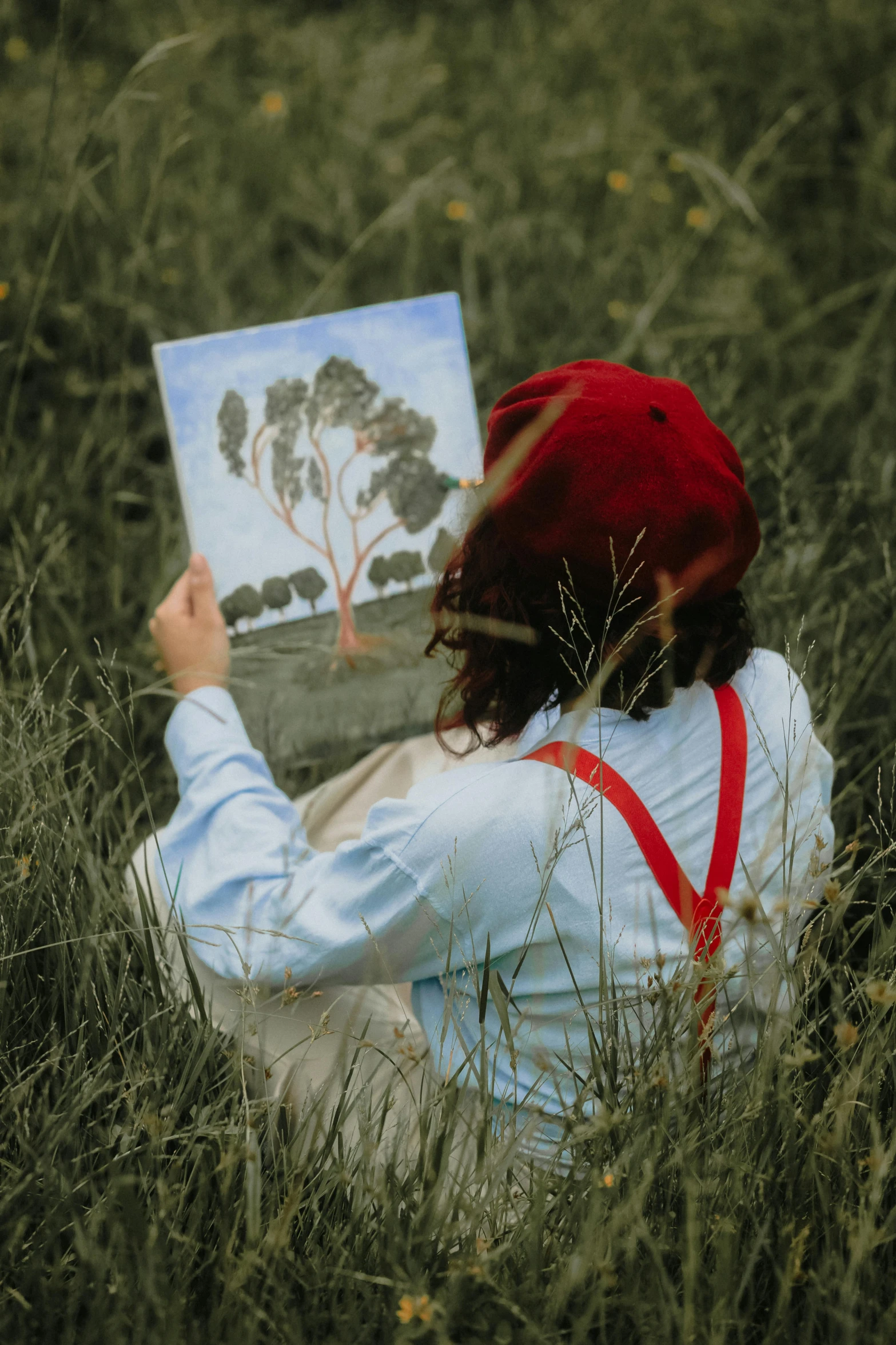 a person is sitting in the grass holding a painting