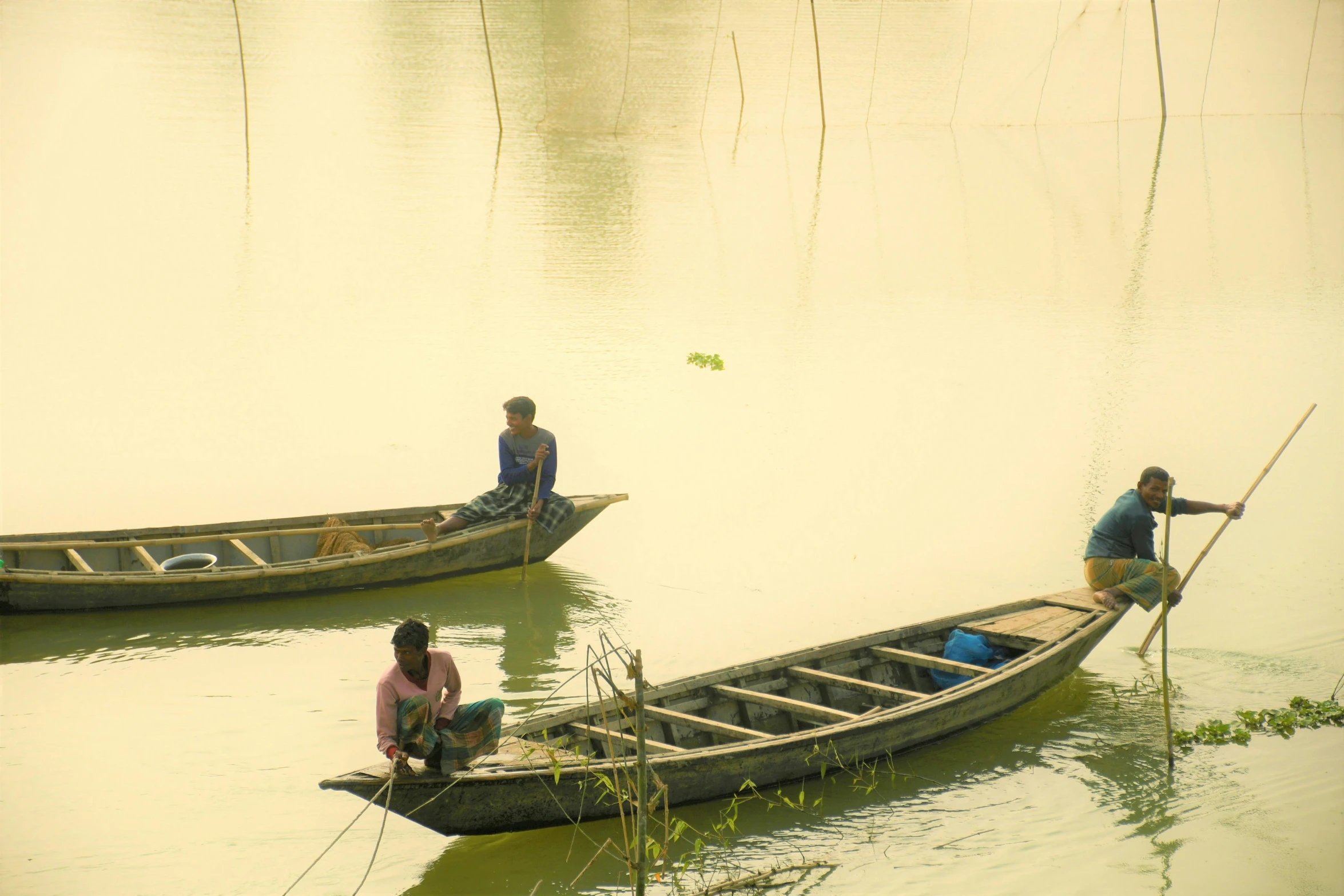 two people in boats with poles and sitting on the water