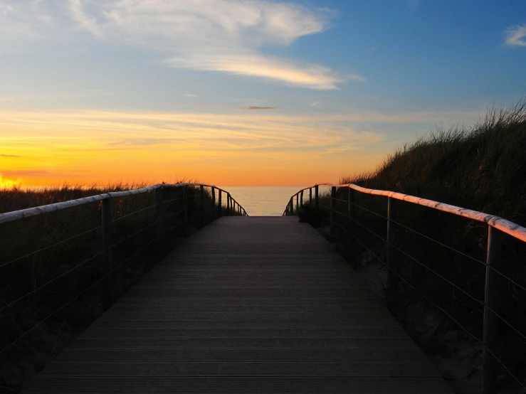 a long boardwalk leading to the ocean at sunset