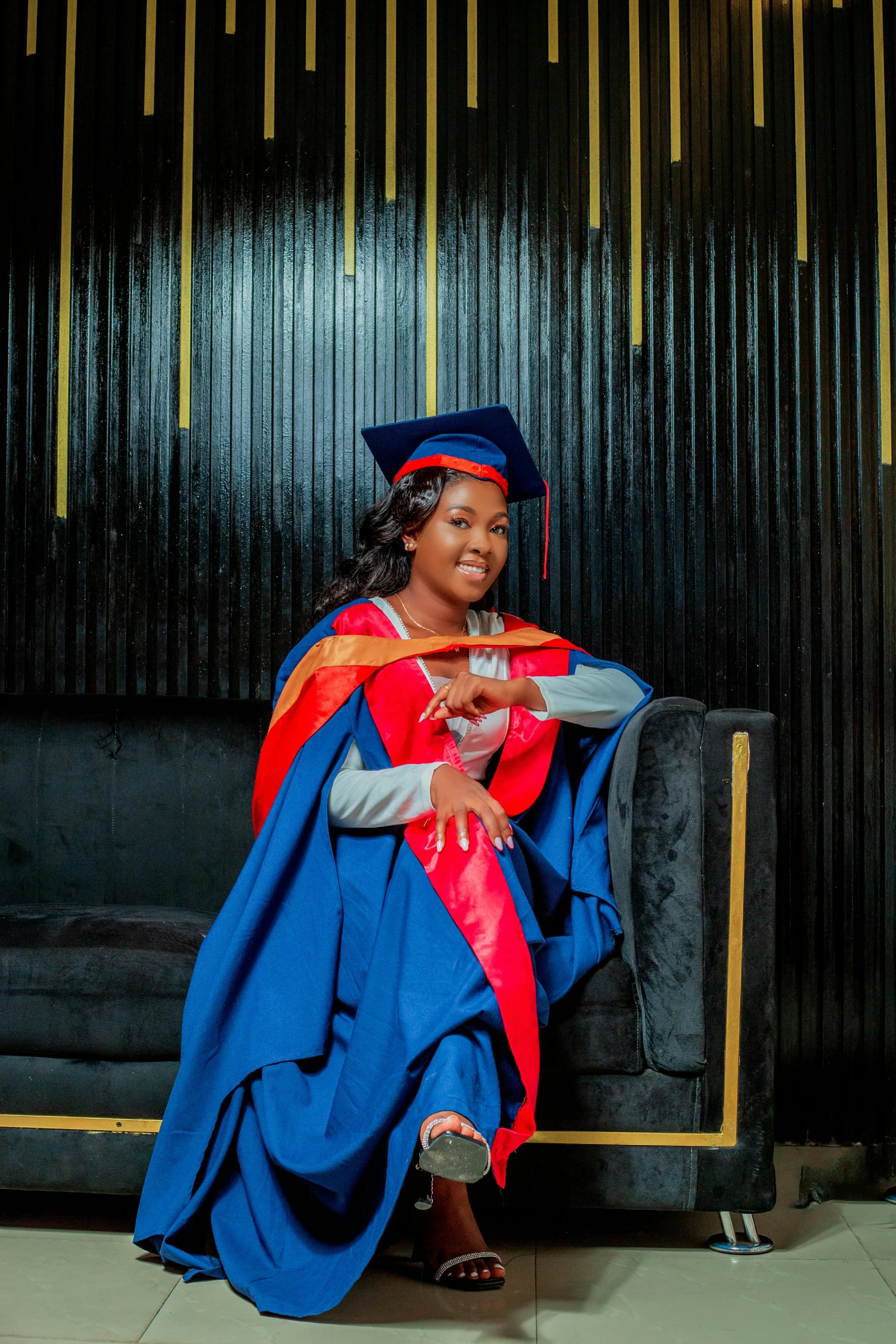 a woman wearing an orange and blue graduation gown sitting on a couch