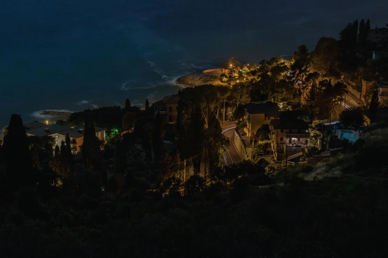 dark night sky view of residential area, with light coming from buildings and hillside with hills in background