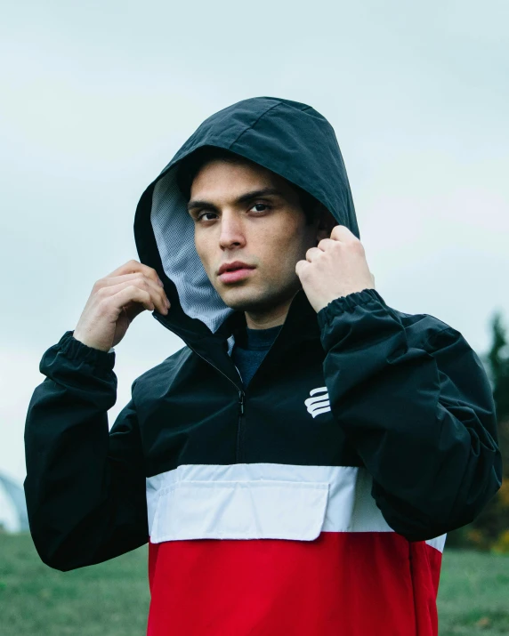 a man in a red and black jacket holding his hoodie over his face