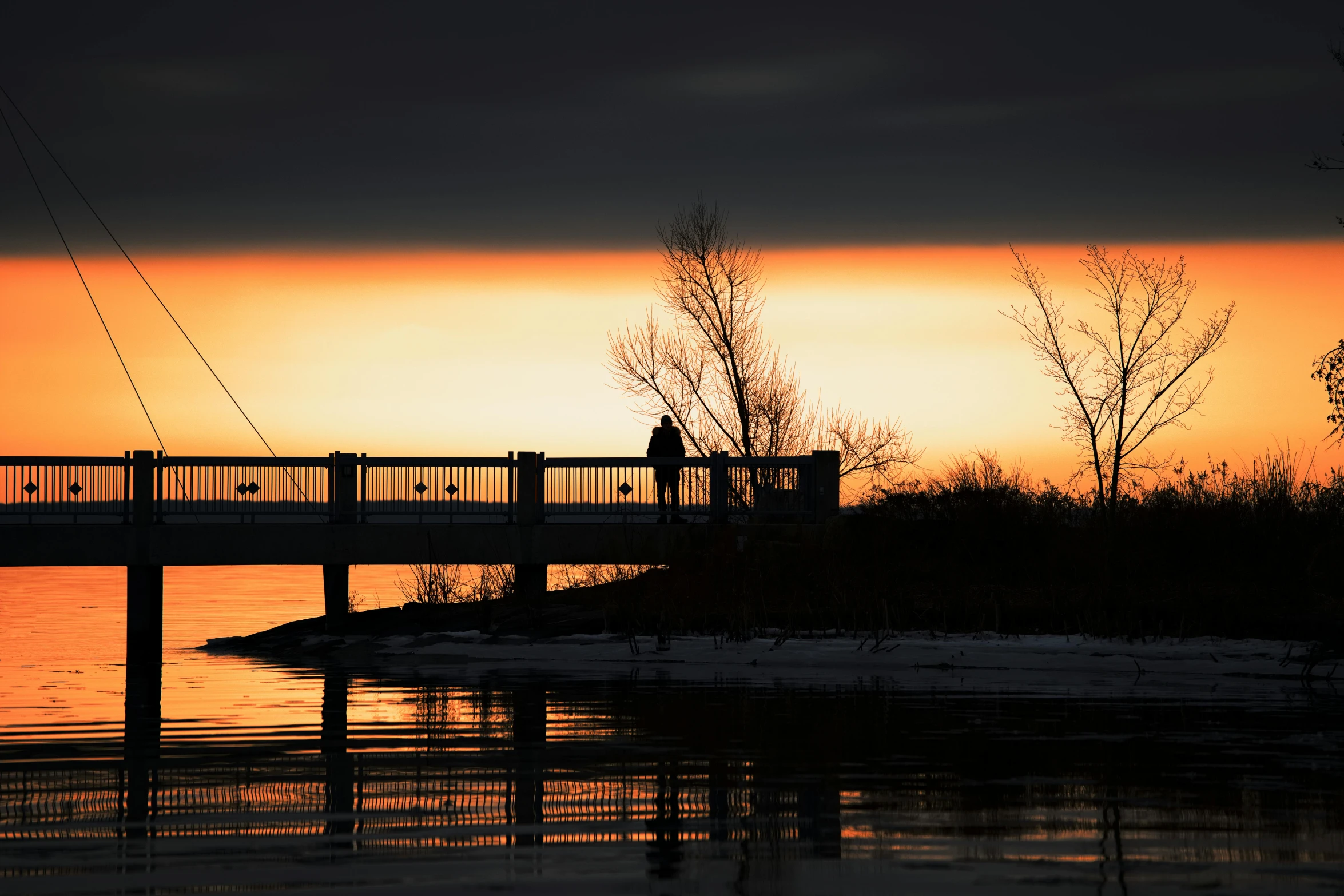 a man is standing on the bridge watching the sunset