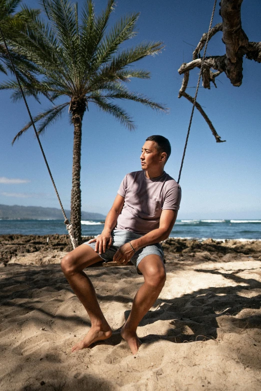 a man sitting on a swing in front of a palm tree