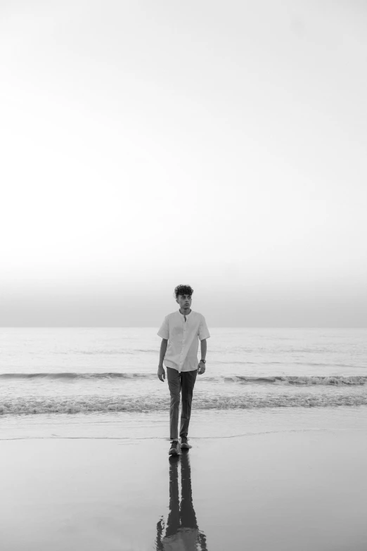 a black and white pograph of a man walking along the beach