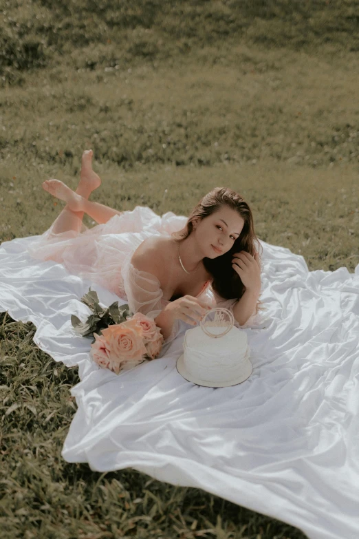 a  woman sitting on a white blanket near a cake