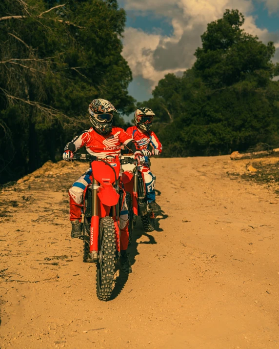 two people ride their dirt bikes down a hill