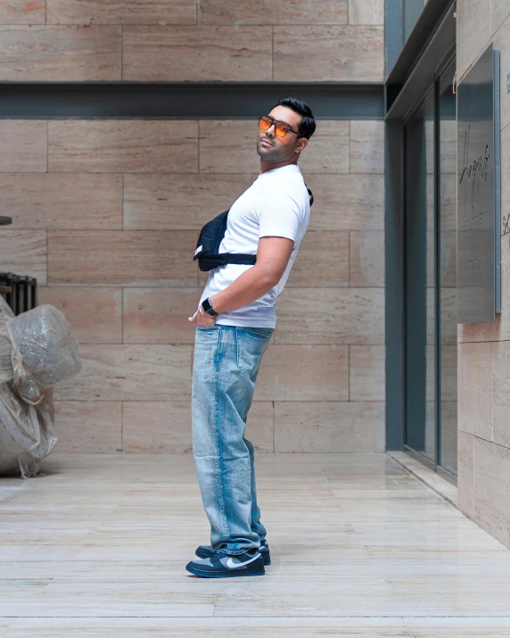 a man poses in front of a wall wearing sunglasses