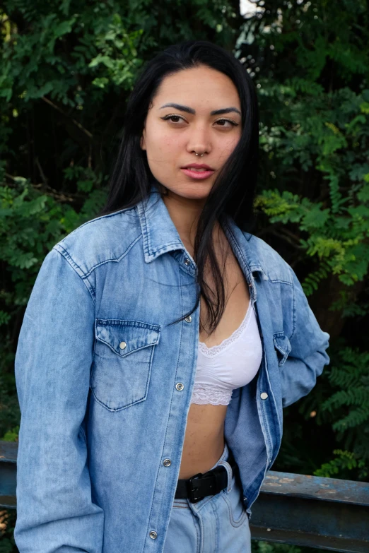 a woman with long black hair and a crop top and jean jacket is posing for a po