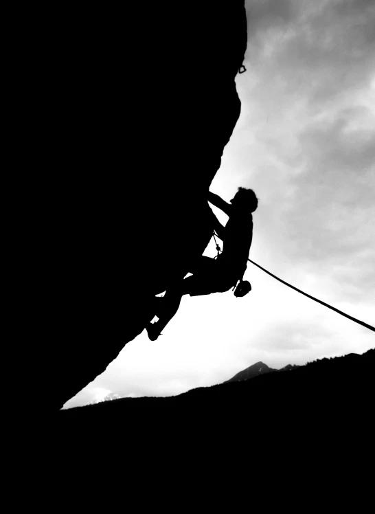 the snowboarder is airborne in the dark, as he tries to rope off the side of the cliff