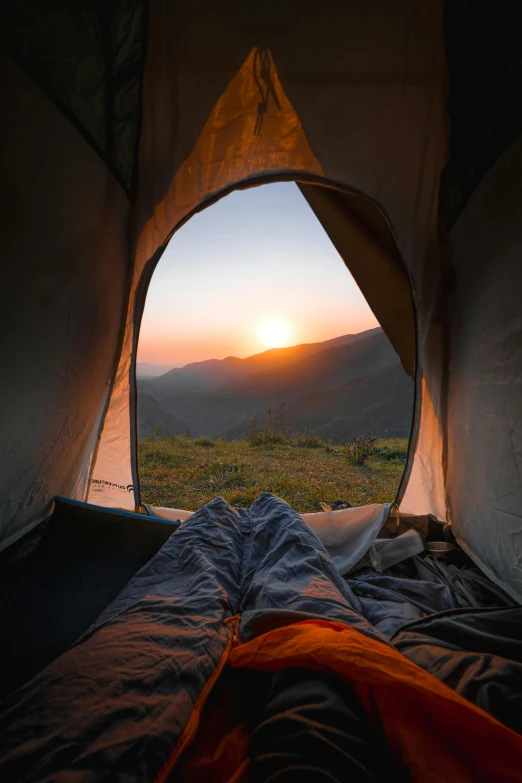 a person is laying down in a tent with the sun setting