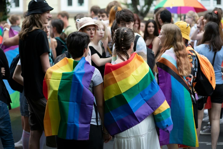 a crowd of people standing around each other holding rainbow colored umbrellas