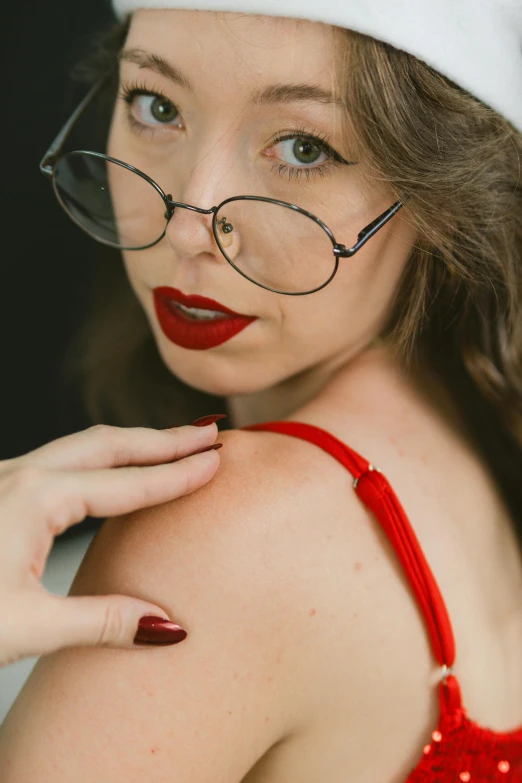 young woman with glasses and red lips wearing a white santa claus hat