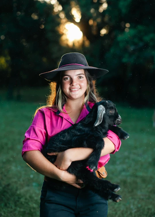 woman in hat and pink shirt holding black dog