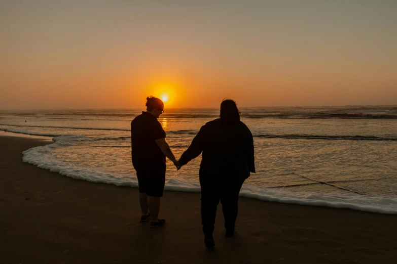 two people are standing near the ocean at sunset