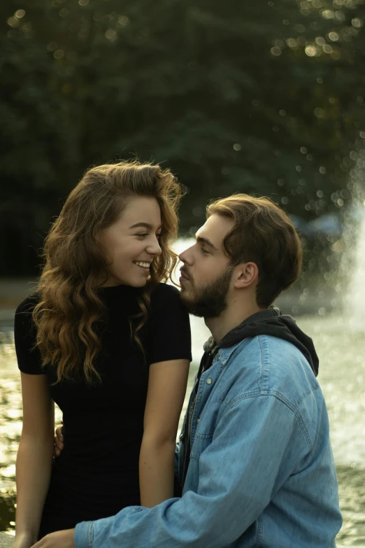 a man and woman smile as they sit on a bench in front of water