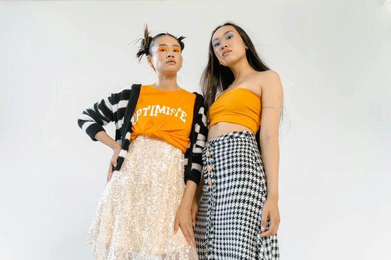 two women wearing orange top and black plaid skirt