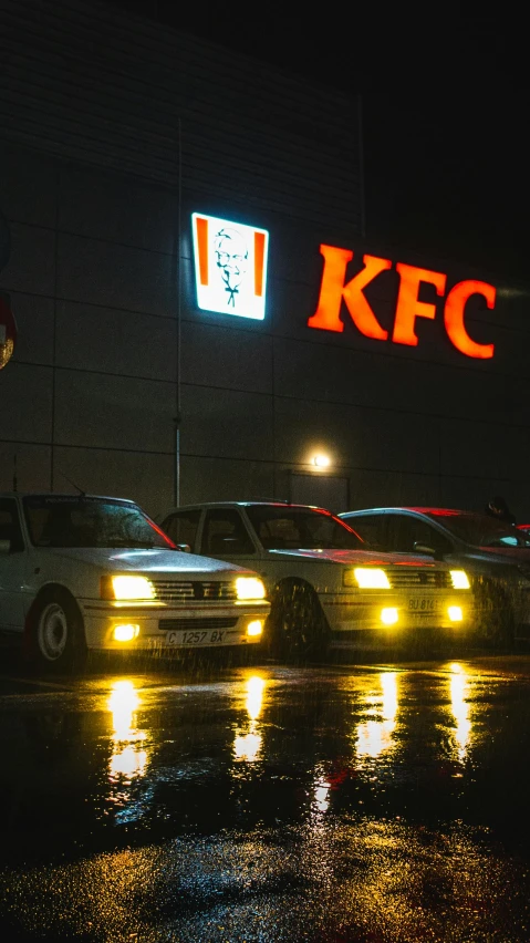 cars driving on a wet street at night in front of kfc