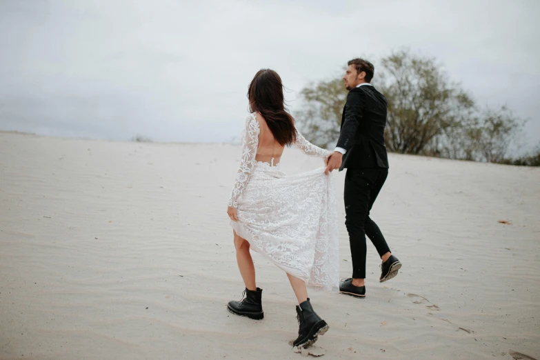 bride in wedding dress and groom with veil walking in the sand dunes