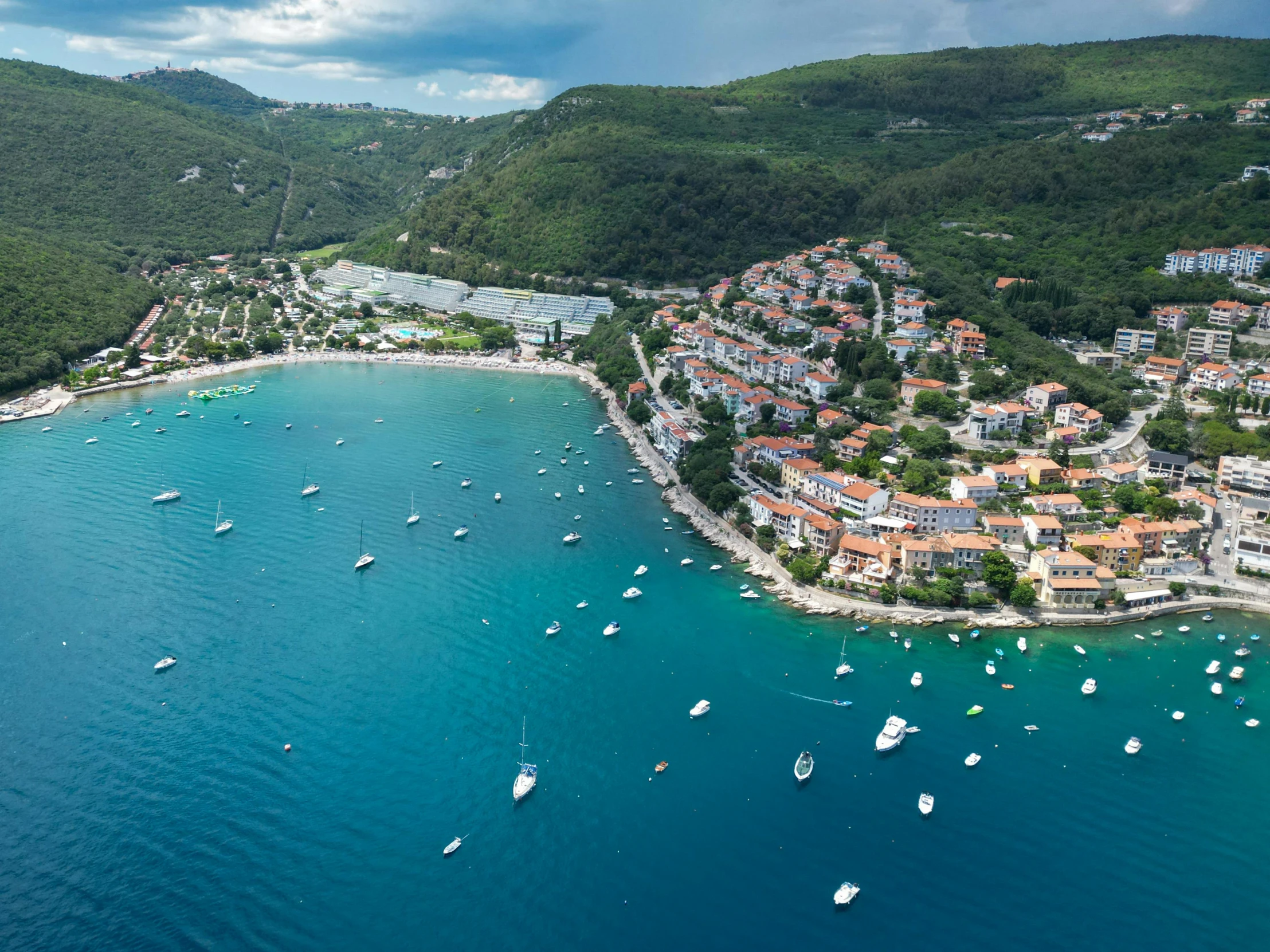 a beach and harbor are seen from above with many small boats