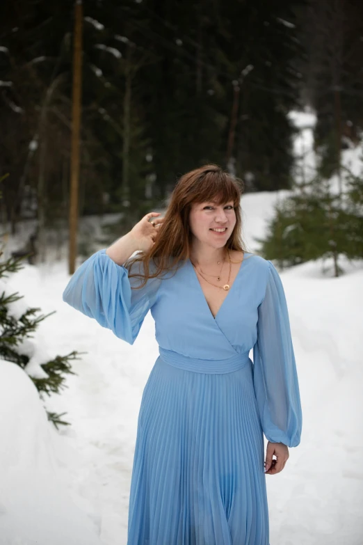 a smiling woman poses in a dress on a snowy day