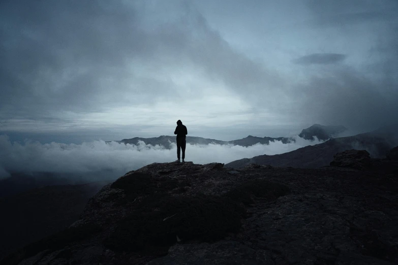 the person stands on a mountain top with their arms out towards a misty valley