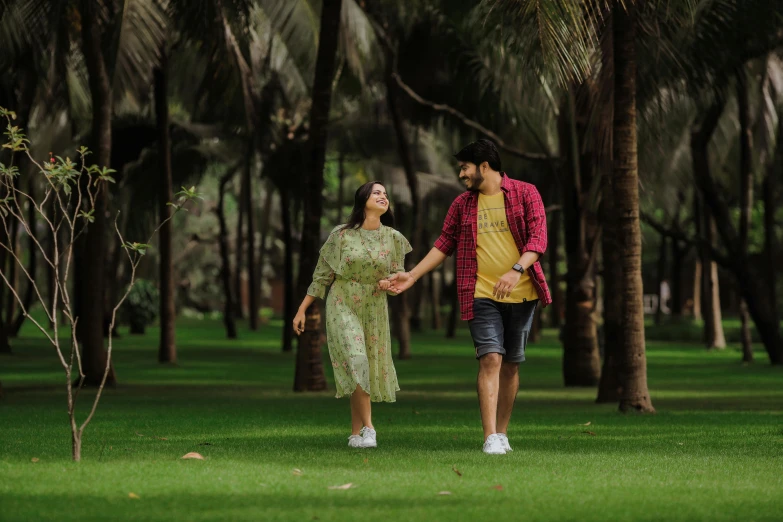 a man and woman walking through an open field with lots of trees