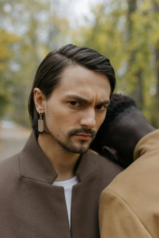 a man wearing earrings in front of some trees