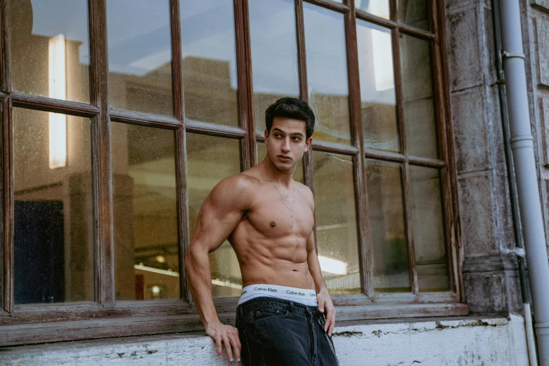 shirtless man posing outside a building with his underwear unoned