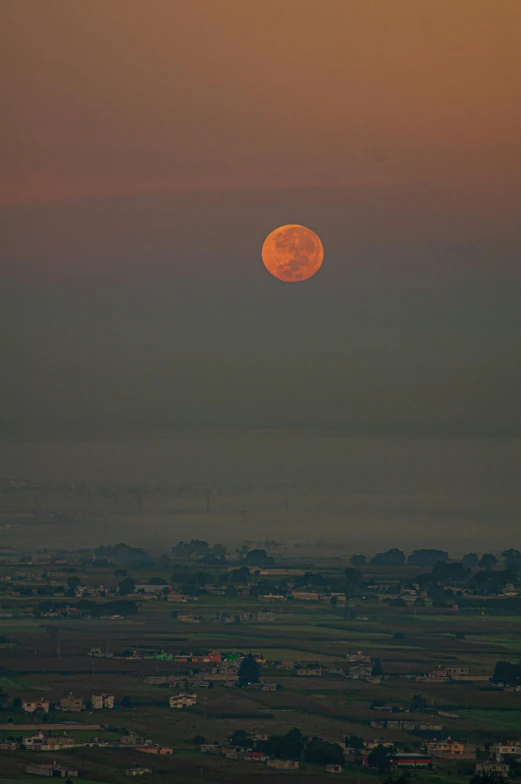an orange and yellow moon setting above the countryside