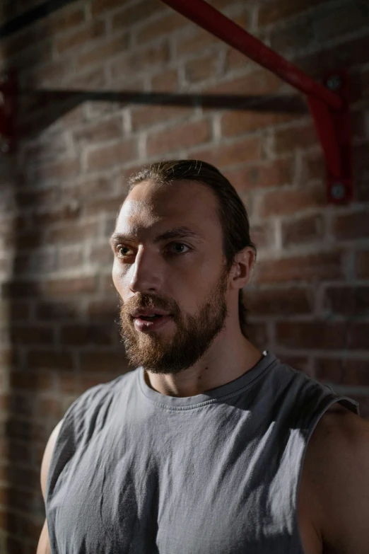 a bearded man is standing by a brick wall