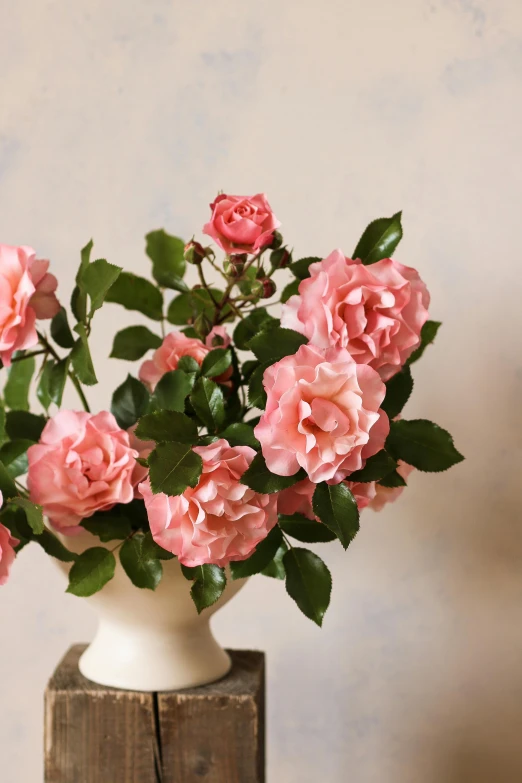 a white vase with pink roses sitting on a wooden table