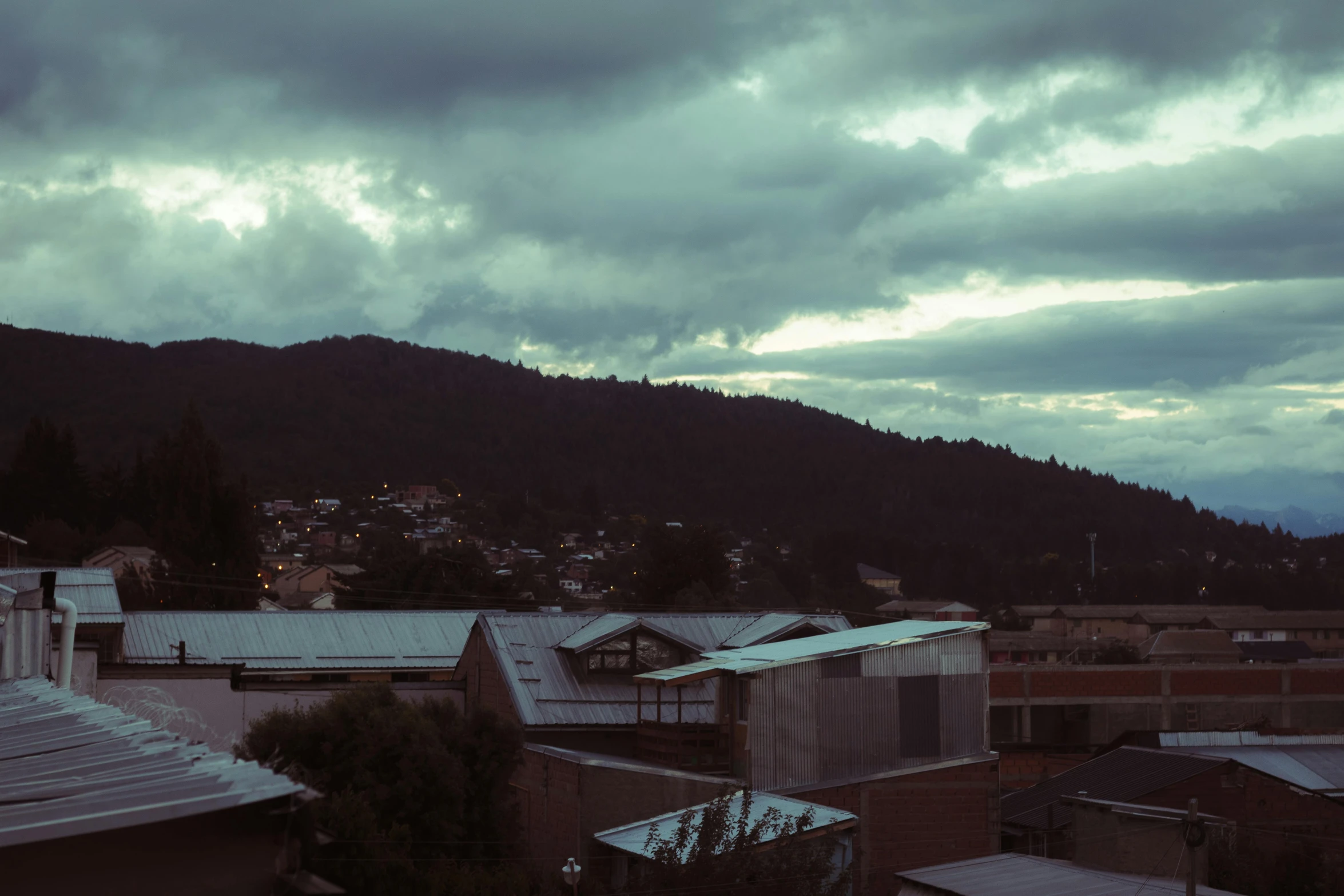 the view from behind the rooftops is of dark clouds, buildings and mountains